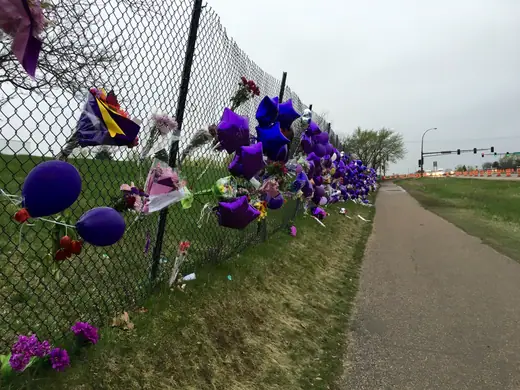 Bouquets, purple balloons and handwritten notes piled against a chain-link fence.