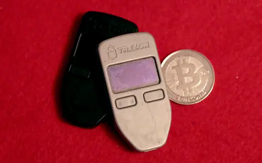 Two Trezor One hardware wallets lying beside a physical Casascius bitcoin token.