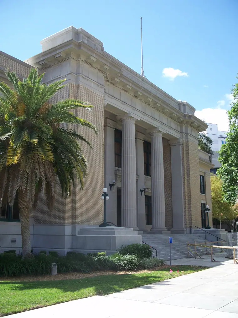 Historic pale stone county courthouse with columns and a pedimented entrance, framed by tropical trees.