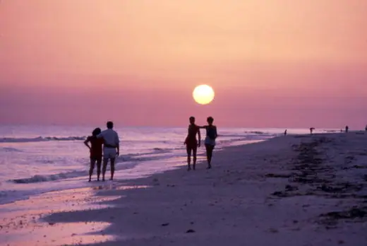 Figures silhouetted on a Gulf beach against a low orange sunset.