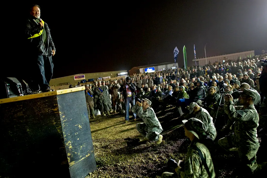 Robin Williams performing on a stage in front of a large crowd of service members at Camp Victory, Iraq.