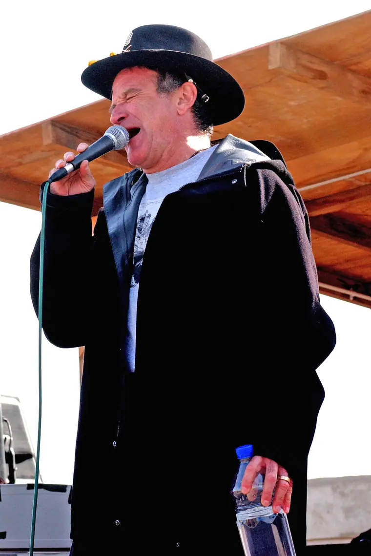 Robin Williams onstage in a T-shirt, arms raised, performing for soldiers at Camp Liberty in Baghdad.