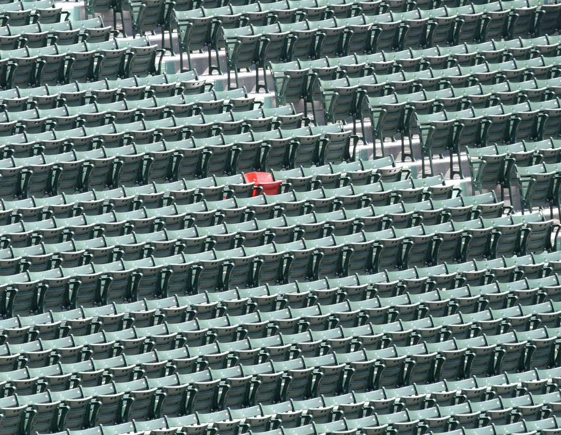A single red seat surrounded by rows of green bleacher seats in a baseball stadium.