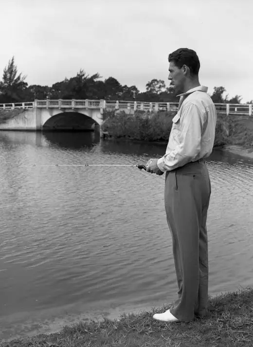 Man in a light shirt holding a fishing rod on a dock, a large fish beside him.