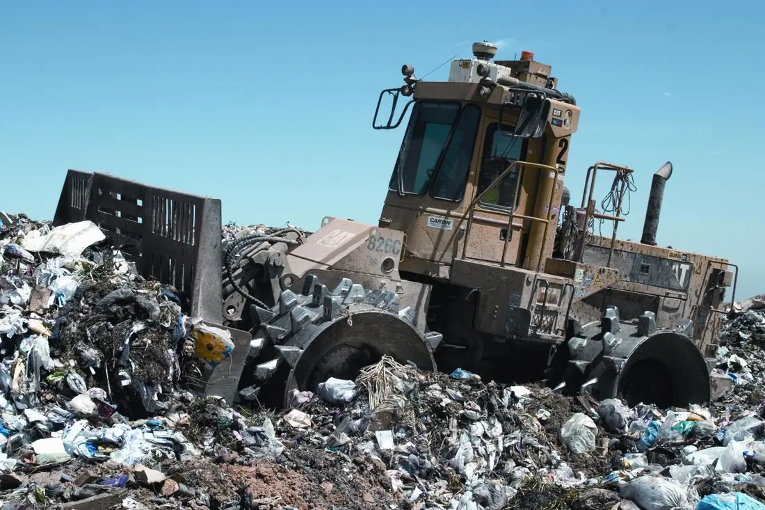 A tracked landfill compactor working across a layer of municipal waste.