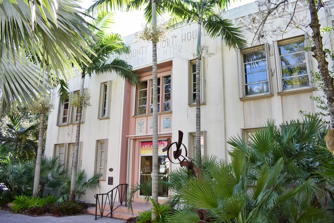 A low 1930s masonry courthouse with an arched entry, palms in front.