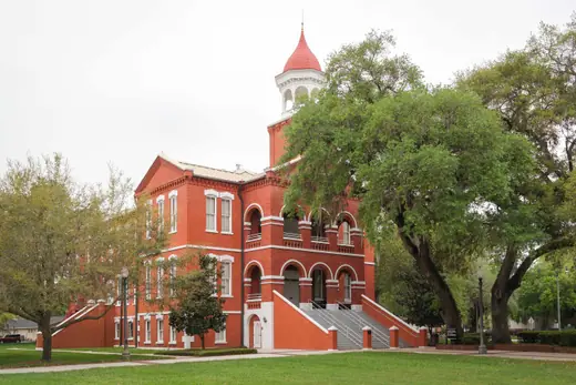 A white nineteenth-century courthouse with a clock tower and covered porch, set among oaks.