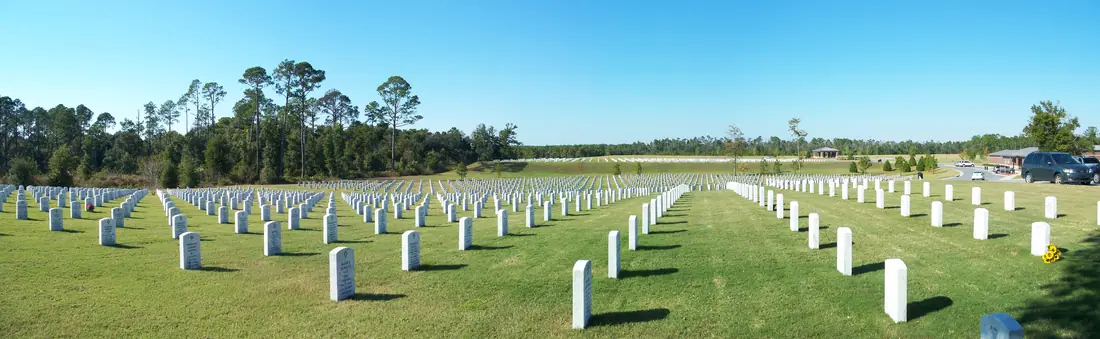 A wide panorama across rows of white headstones and lawn at Barrancas National Cemetery.
