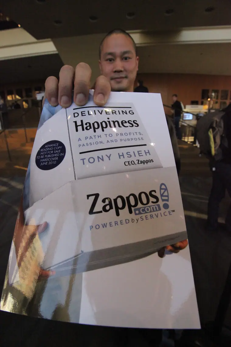 Tony Hsieh holding up a copy of his book at a conference.