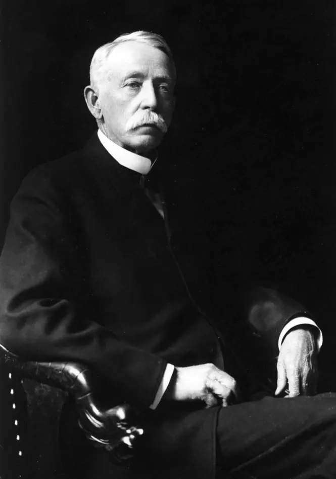 Seated studio portrait of an elderly man with a heavy white beard in a dark three-piece suit.
